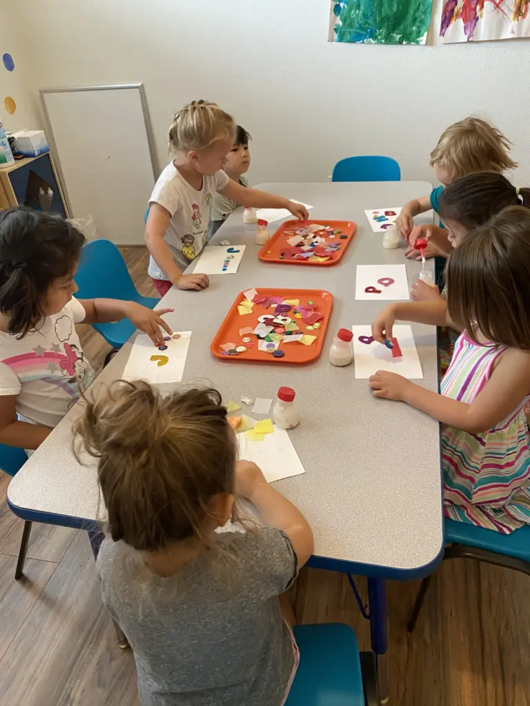 Children work on red and yellow art projects on orange trays around a table