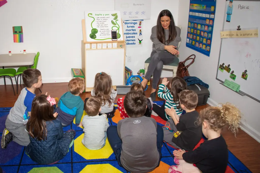 Children sit cross-legged on the bright alphabet rug for circle time with their teacher