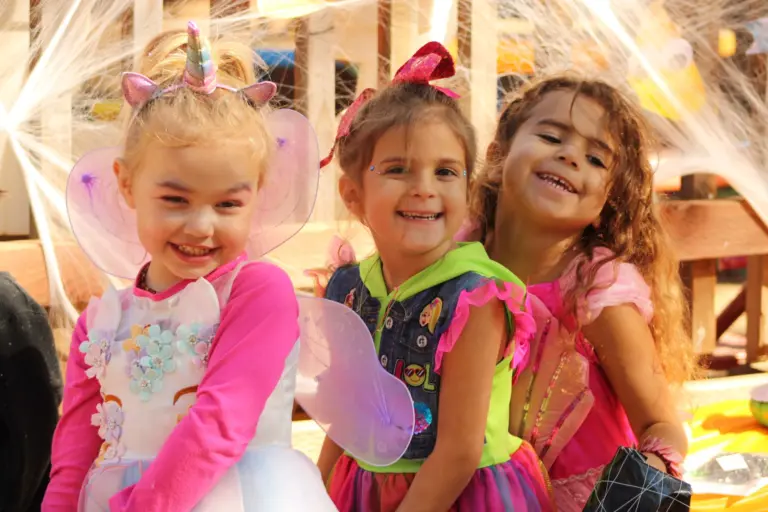 Three smiling girls in fairy wings and a unicorn headband pose together