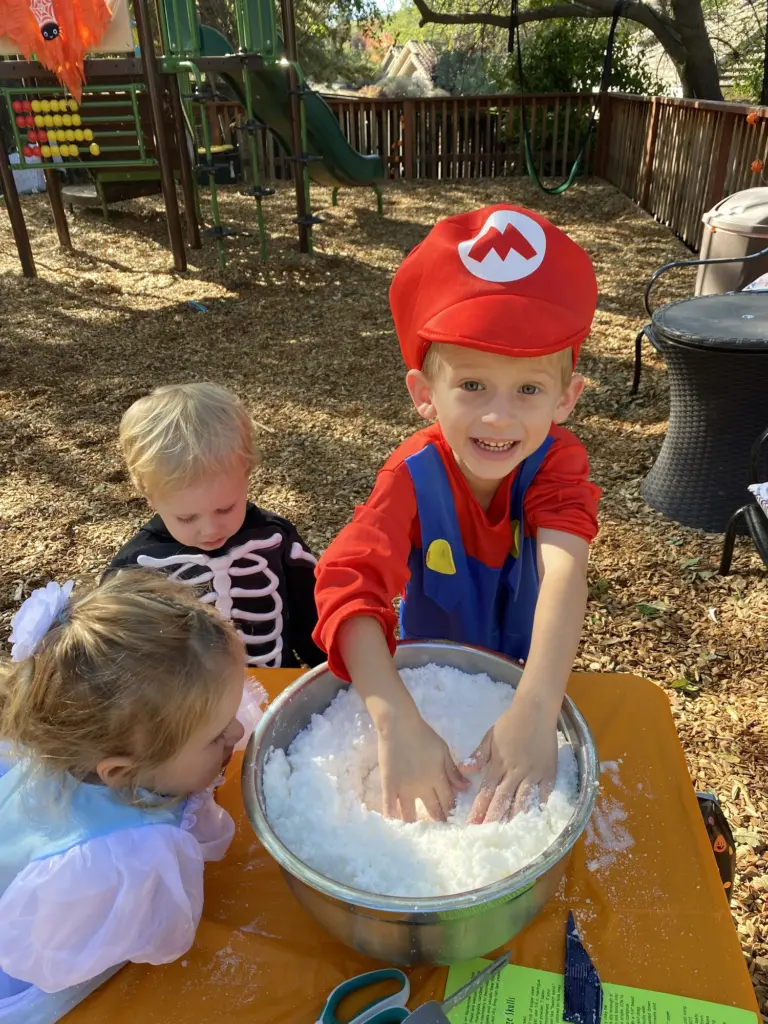A boy dressed as Mario stirs a big bowl of white goo with friends