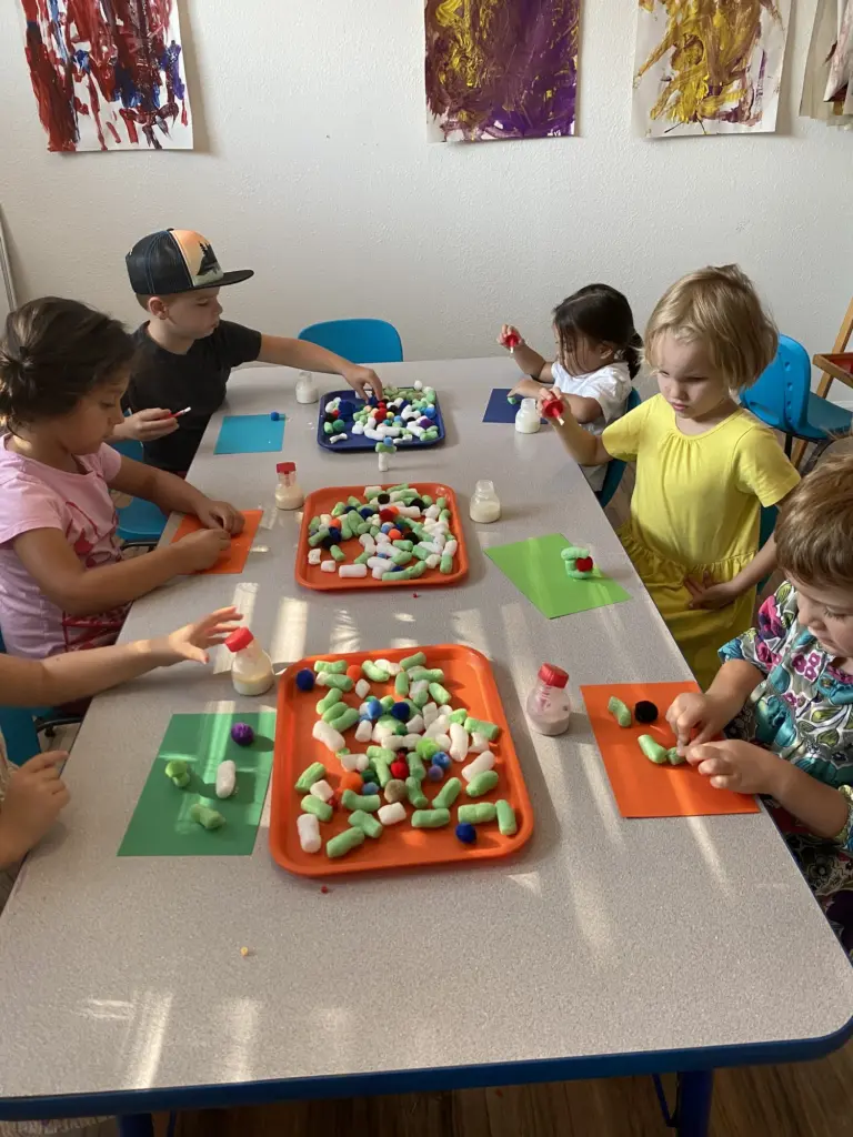 Children press colourful shapes into mosaics at a long table