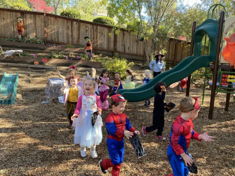 Children in costumes, including two Spider-Men, parade across the play yard
