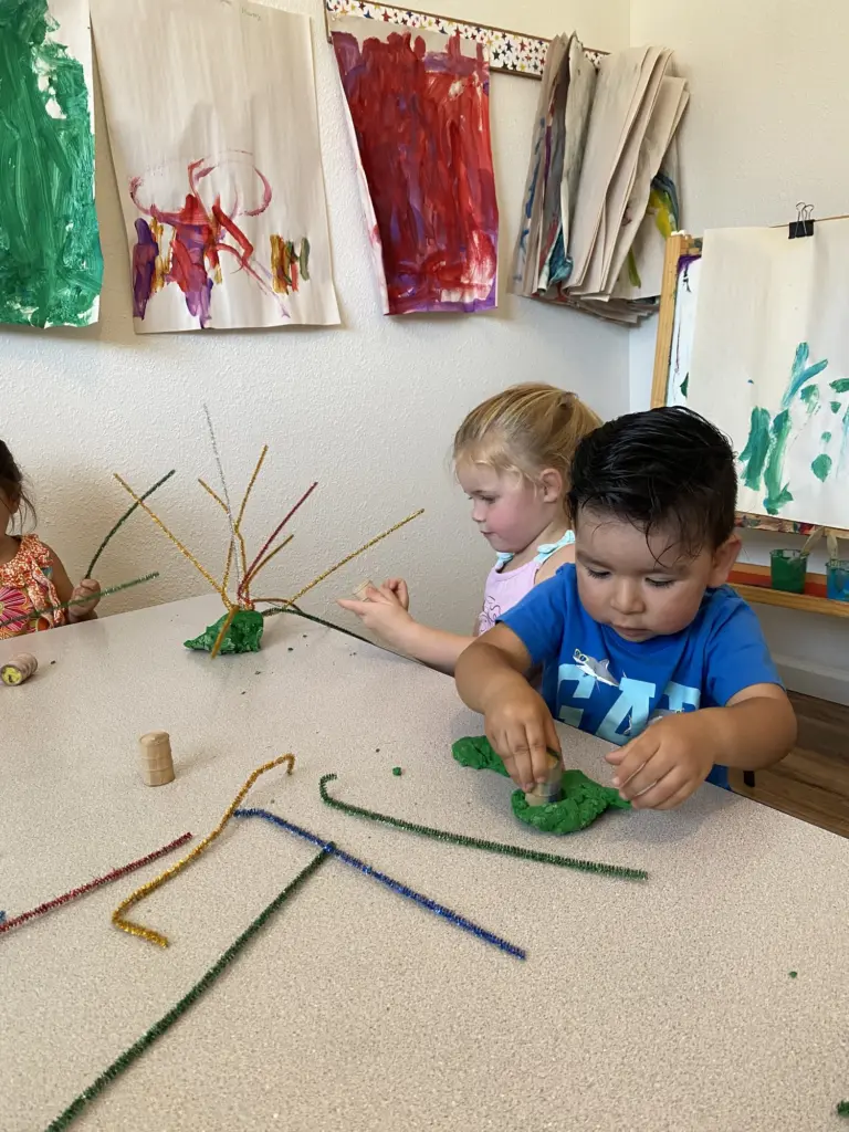 Two children twist colourful pipe cleaners and sticks into sculptures