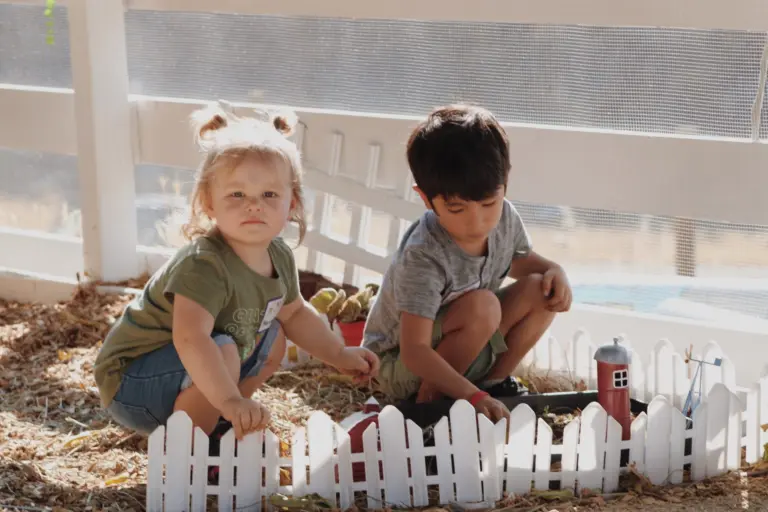 Two toddlers plant flowers in a little fenced garden bed