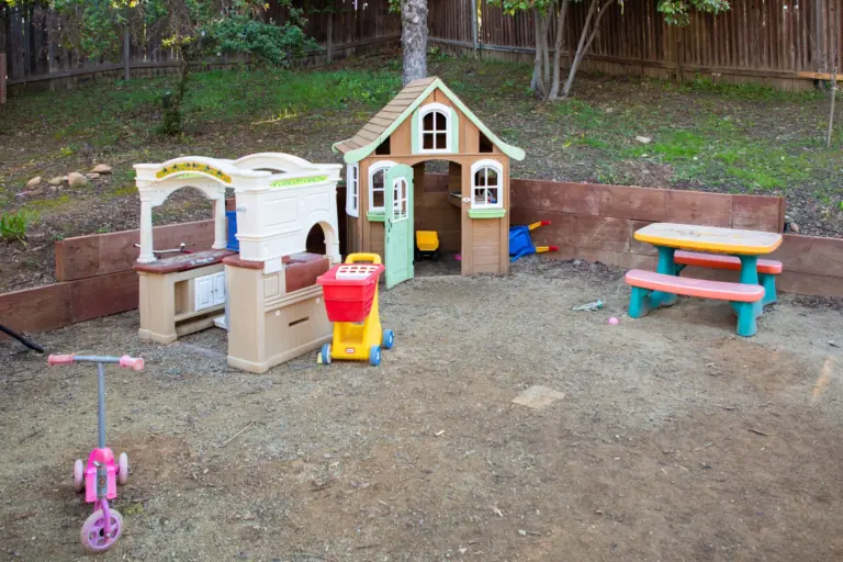 An outdoor play kitchen and a little cottage playhouse on a sandy patch of the yard