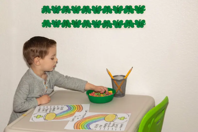 A boy works on a rainbow worksheet at his own little table with a bowl of counters