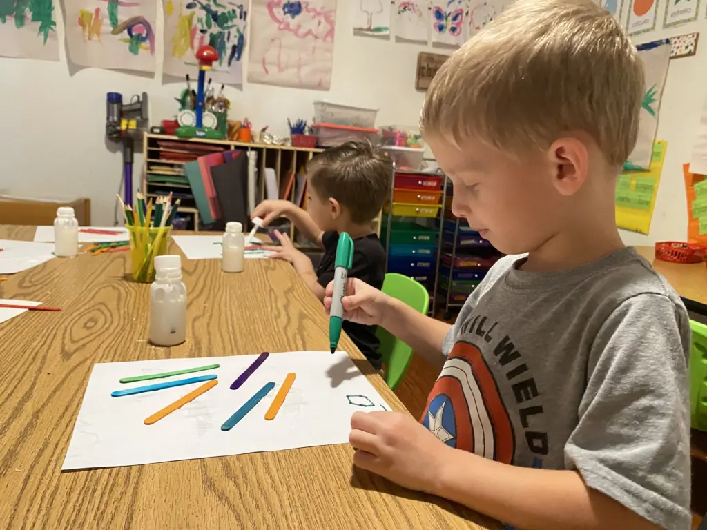 A boy draws with markers at a classroom table during space week