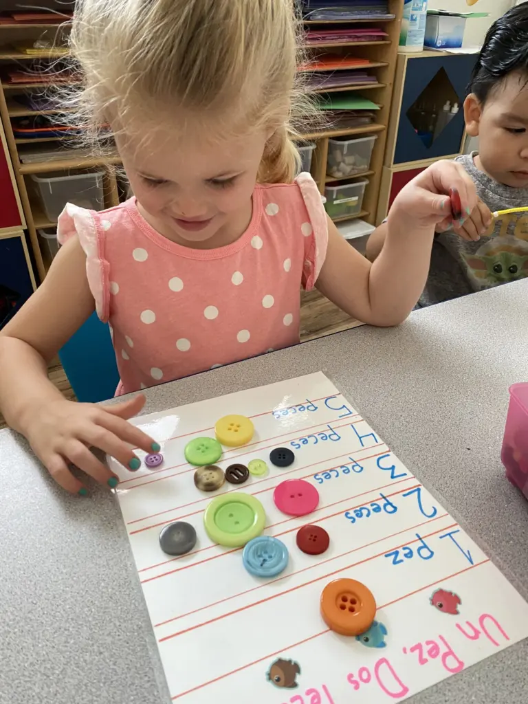 A little girl places coloured buttons on a counting sheet with Spanish number words