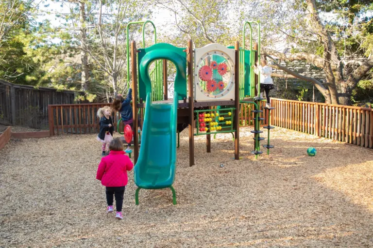 Children run across the wood chips toward the play structure